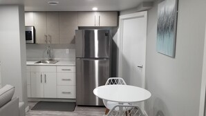 Una cocina compacta con armarios blancos, un refrigerador de acero inoxidable, un lavamanos y un pequeño comedor.