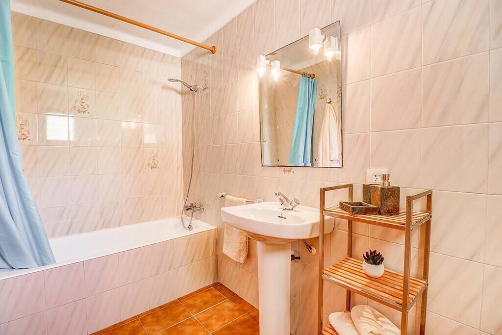 Et badeværelse med badekar, vask, spejl og en hylde med toiletartikler.