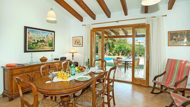 A dining area with a wooden table and chairs, a buffet counter, and a view of a swimming pool through glass doors. - Villa Almendra Boi, Mallorcan country house with modern touches (Pollença)