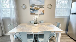 Een eetkamer met een houten tafel, lichtblauwe stoelen, een schilderij aan de muur en een koelkast.