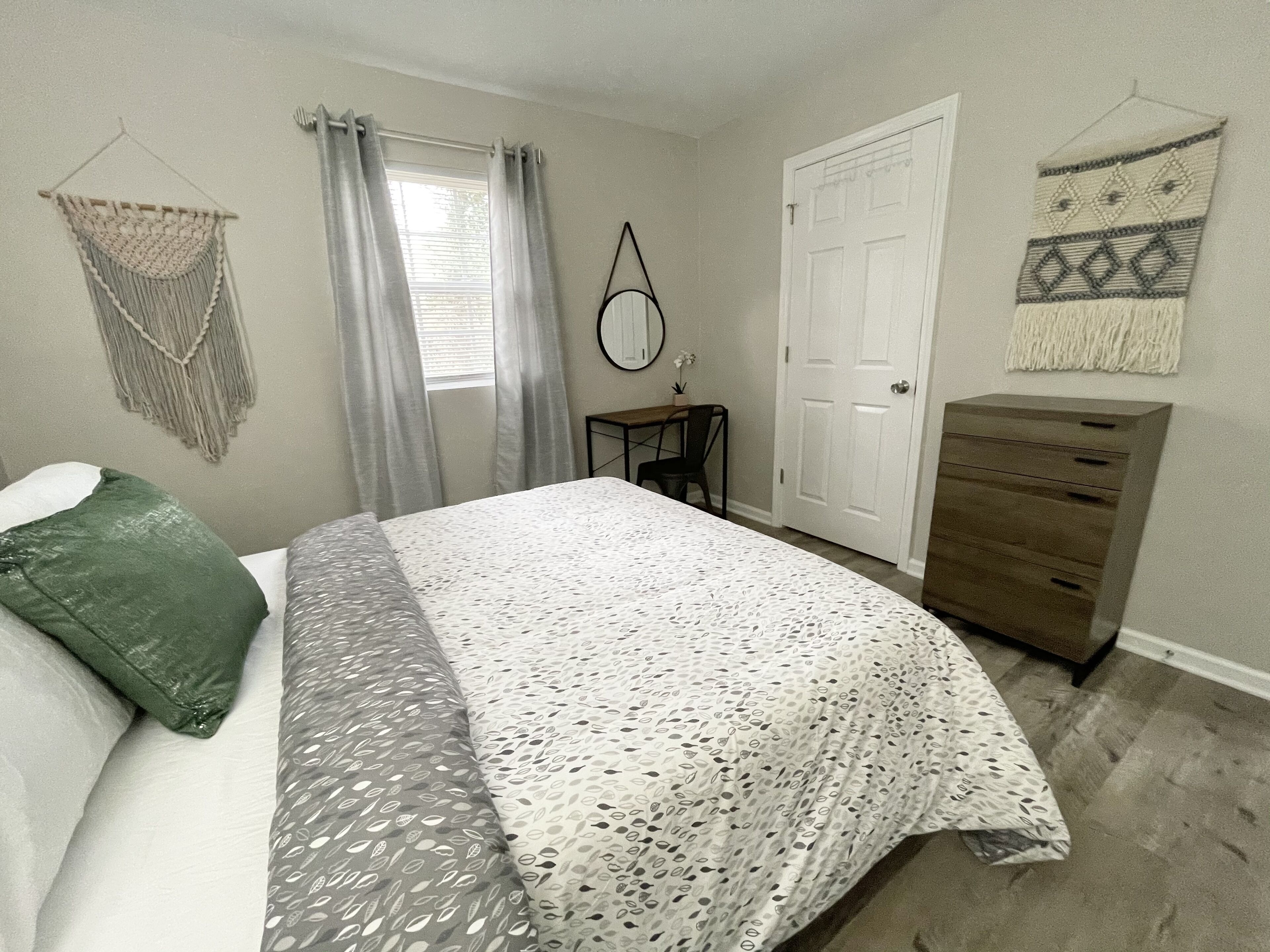 Un dormitorio con cama, cómoda, escritorio y puerta.