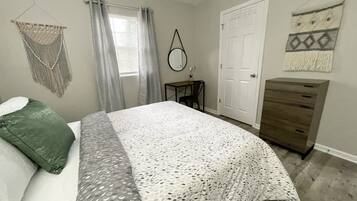 Un dormitorio con cama, cómoda, escritorio y puerta.