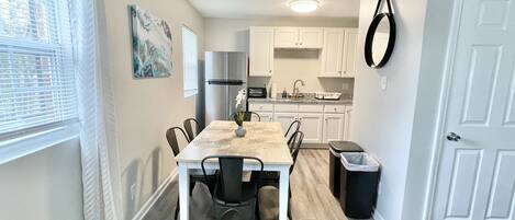 Una cocina funcional con armarios blancos, un refrigerador de acero inoxidable y una mesa de comedor con sillas.