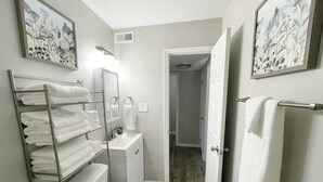 Une salle de bain équipée de toilettes, d’un lavabo, d’un porte-serviettes et de deux tableaux représentant des motifs floraux.