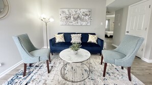 Un salon avec un canapé bleu, deux fauteuils, une table basse ronde et un lampadaire.