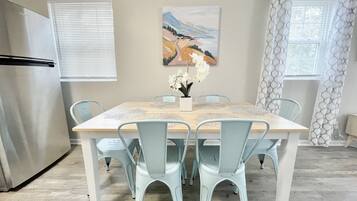 Un coin repas avec une table en bois, des chaises bleu clair, un vase blanc orné de fleurs et un tableau accroché au mur.