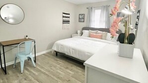 Une chambre à coucher avec un lit, un bureau, une chaise, un miroir et un vase rempli de fleurs.