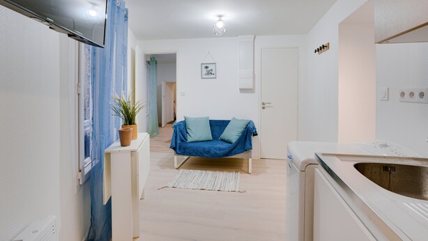 A compact kitchen with a built-in oven, a sink, and a blue sofa in the center. - La Bridole - Apt rénové proche Gare (Vitré)