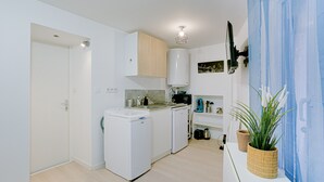 A compact kitchen with white appliances, a wooden cabinet, and a potted plant. - La Bridole - Apt rénové proche Gare (Vitré)