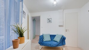 A modern, minimalist room with a blue sofa, a small table with a plant, and a door leading to another room. - La Bridole - Apt rénové proche Gare (Vitré)