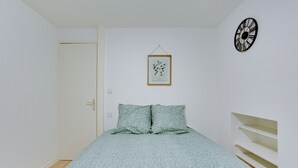 A bedroom with a bed, a door, a framed botanical print, and a wall clock. - La Bridole - Apt rénové proche Gare (Vitré)