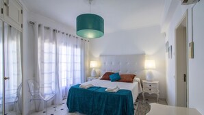 A bedroom with a bed, two bedside tables, a clear chair, a teal lamp, and a white ceiling. - Villa Brisa do Mar | 4 Bedrooms | Walking Distance | Galé (Galé)