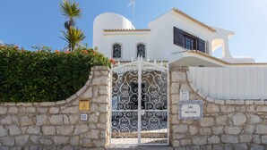 A white building with a stone wall, a metal gate, and a palm tree. - Villa Brisa do Mar | 4 Bedrooms | Walking Distance | Galé (Galé)
