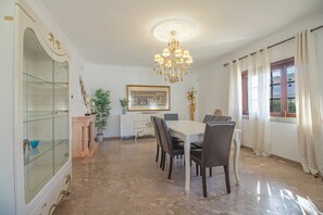 Un coin repas agrémenté d’un lustre, d’une table, de chaises, d’une vitrine et d’une fenêtre avec des rideaux.