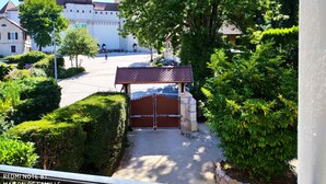 Un patio con entrada porticada, un pequeño pabellón y un árbol grande.