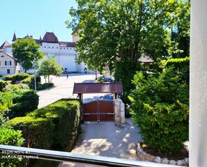 A courtyard with a gated entrance, a small pavilion, and a large building with multiple towers in the background.