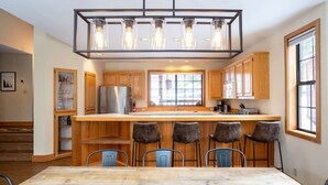 A modern kitchen with a wooden island, bar stools, and a hanging light fixture.