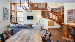A spacious living area with a wooden staircase, a dining table, and a comfortable seating arrangement.