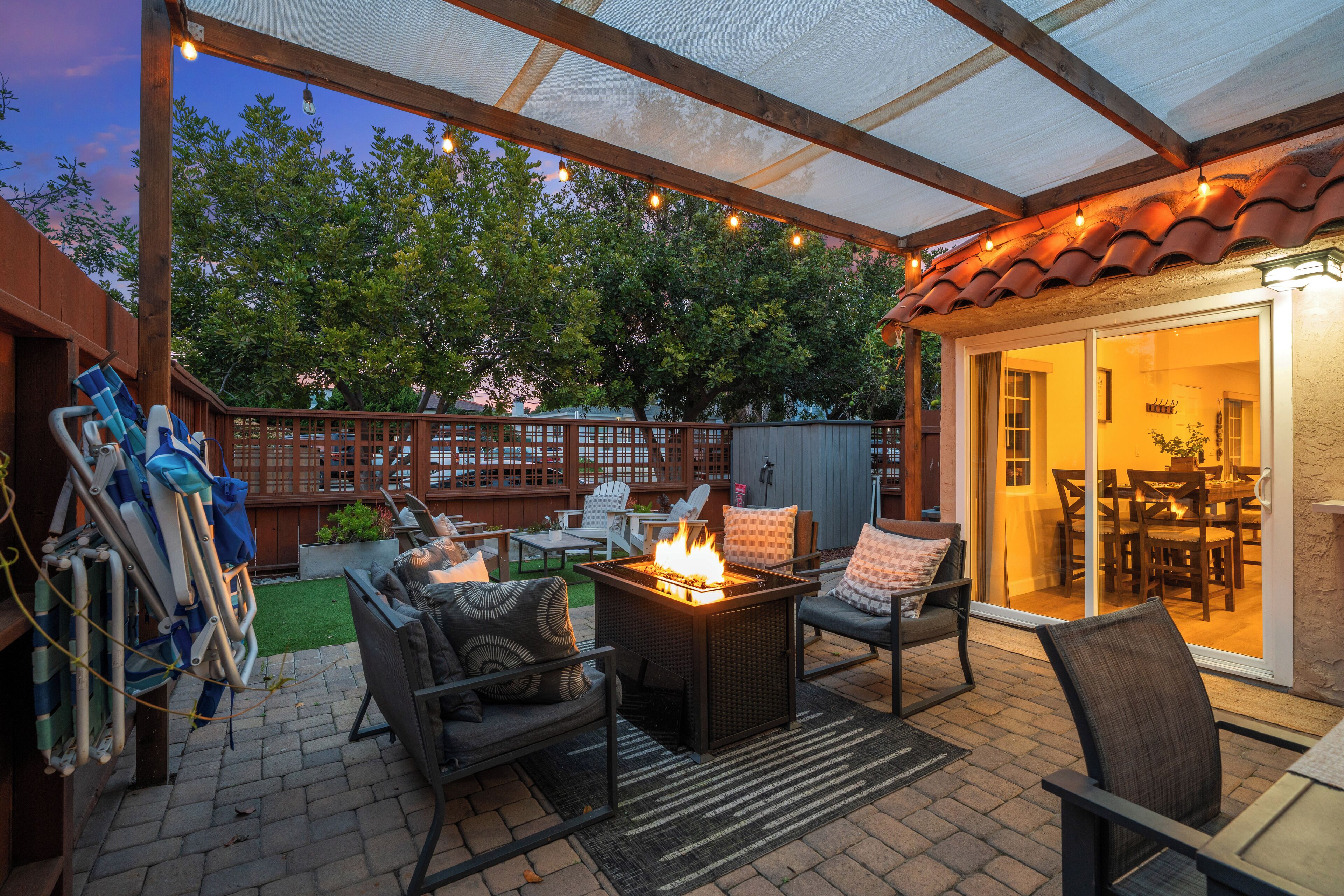 An outdoor patio with a fire feature, seating, and a covered area with string lights.