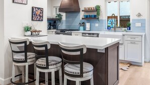 Een moderne keuken met een centraal eiland, barkrukken, hanglampen en een gastvrij bord.