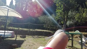 Eine Person entspannt sich im Liegestuhl draußen, mit einem Zelt und Grünpflanzen im Hintergrund.