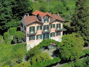 Une maison à plusieurs étages, avec un toit recouvert de tuiles rouges, des volets verts et un jardin.