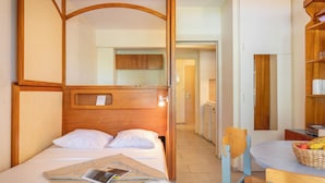 A room with a bed, a wooden headboard, a table with a basket of fruit, and a chair. - Résidence Pierre & Vacances Hyeres Le Port (Hyères)