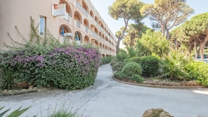 A hotel with a multi-story structure, outdoor seating area, and a garden with various plants and trees. - Résidence Pierre & Vacances Hyeres Le Port (Hyères)