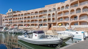 A marina with several boats docked, a building with multiple balconies, and a clear blue sky. - Résidence Pierre & Vacances Hyeres Le Port (Hyères)