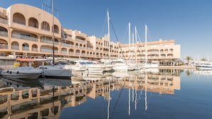 A marina with multiple boats docked, a building with arched balconies, and clear reflections in the calm water. - Résidence Pierre & Vacances Hyeres Le Port (Hyères)