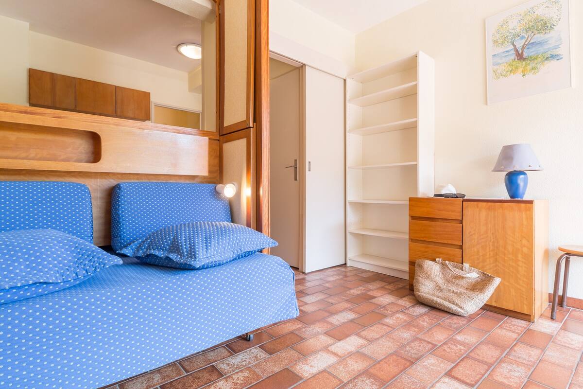 Ein Zimmer mit einem Bett, einem Holzschrank, einer Lampe und einer Tür.