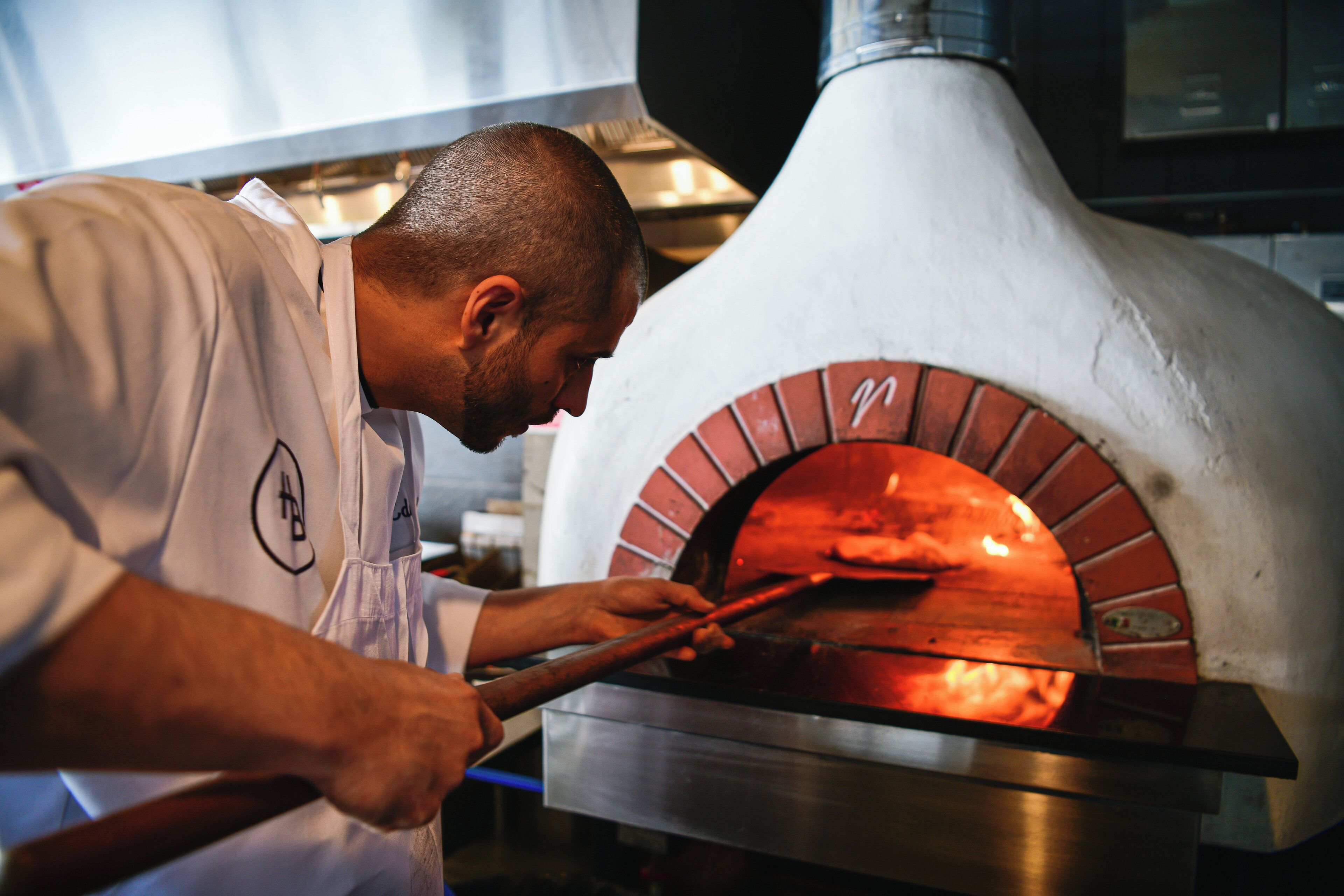 Un chef utilise un ustensile à long manche pour manipuler les pizzas dans un four à briques.