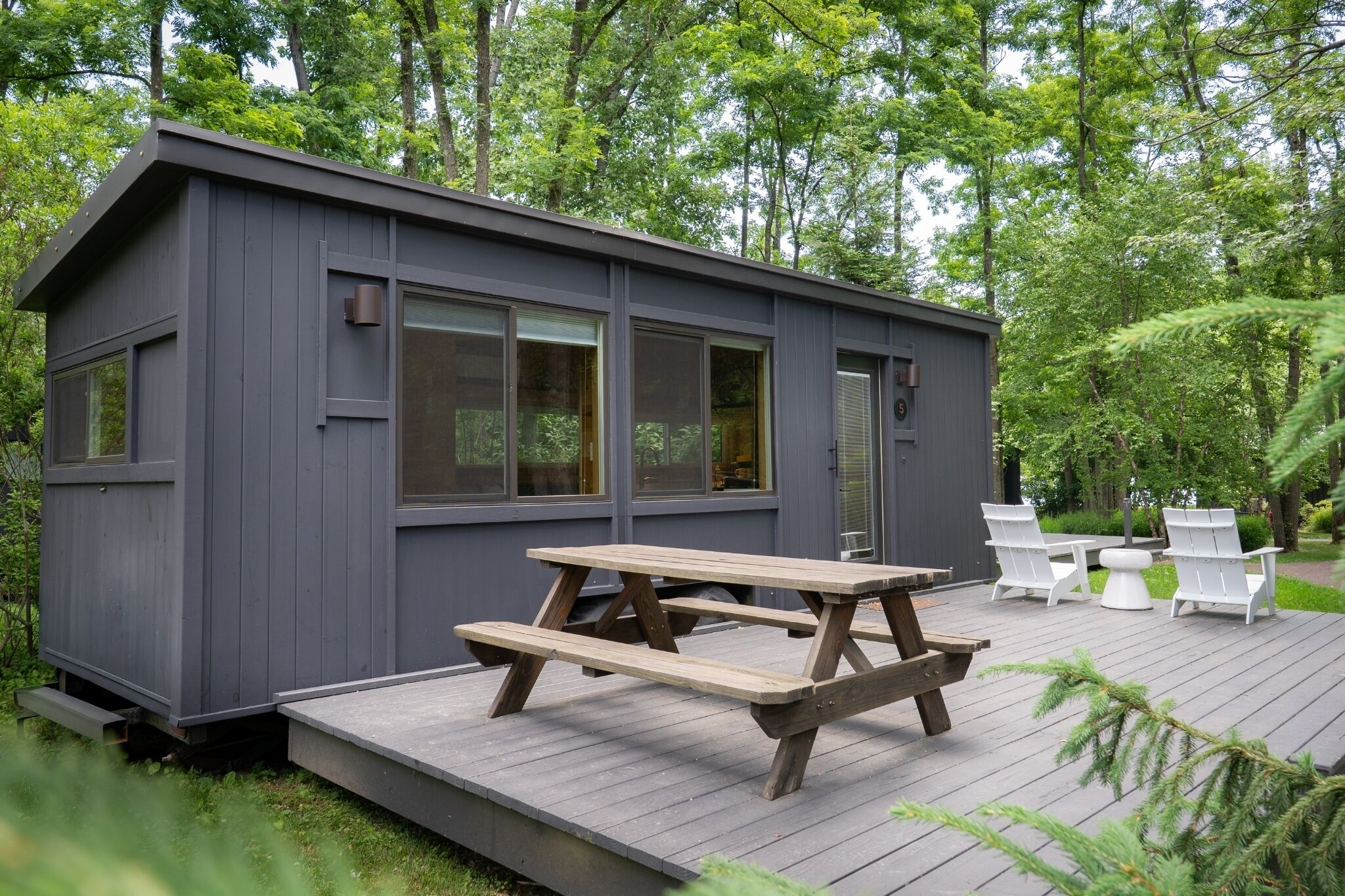 Una cabaña pequeña con una terraza de madera, una mesa de picnic y mobiliario exterior.