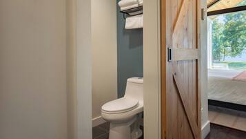A bathroom with a toilet, a towel rack, and a view of a bed and a window.