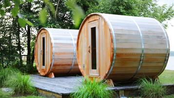 Two wooden barrel-shaped cabins with doors, set on a wooden platform in a grassy area with trees in the background.