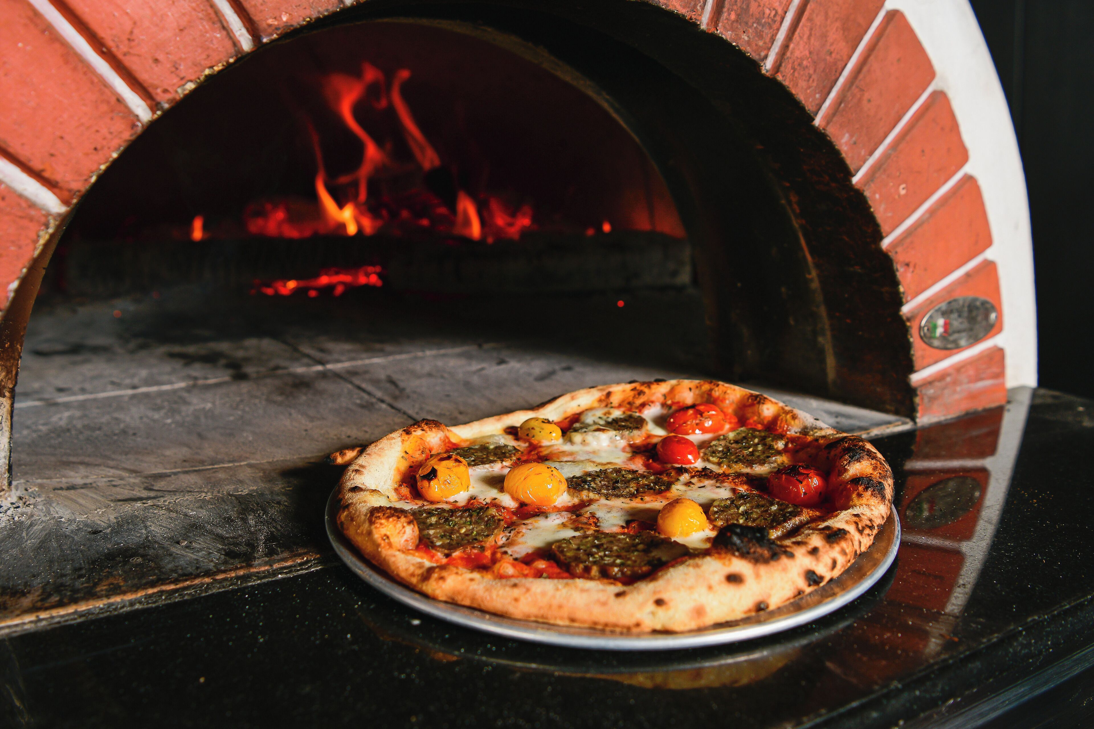 A pizza in a brick oven with visible flames.