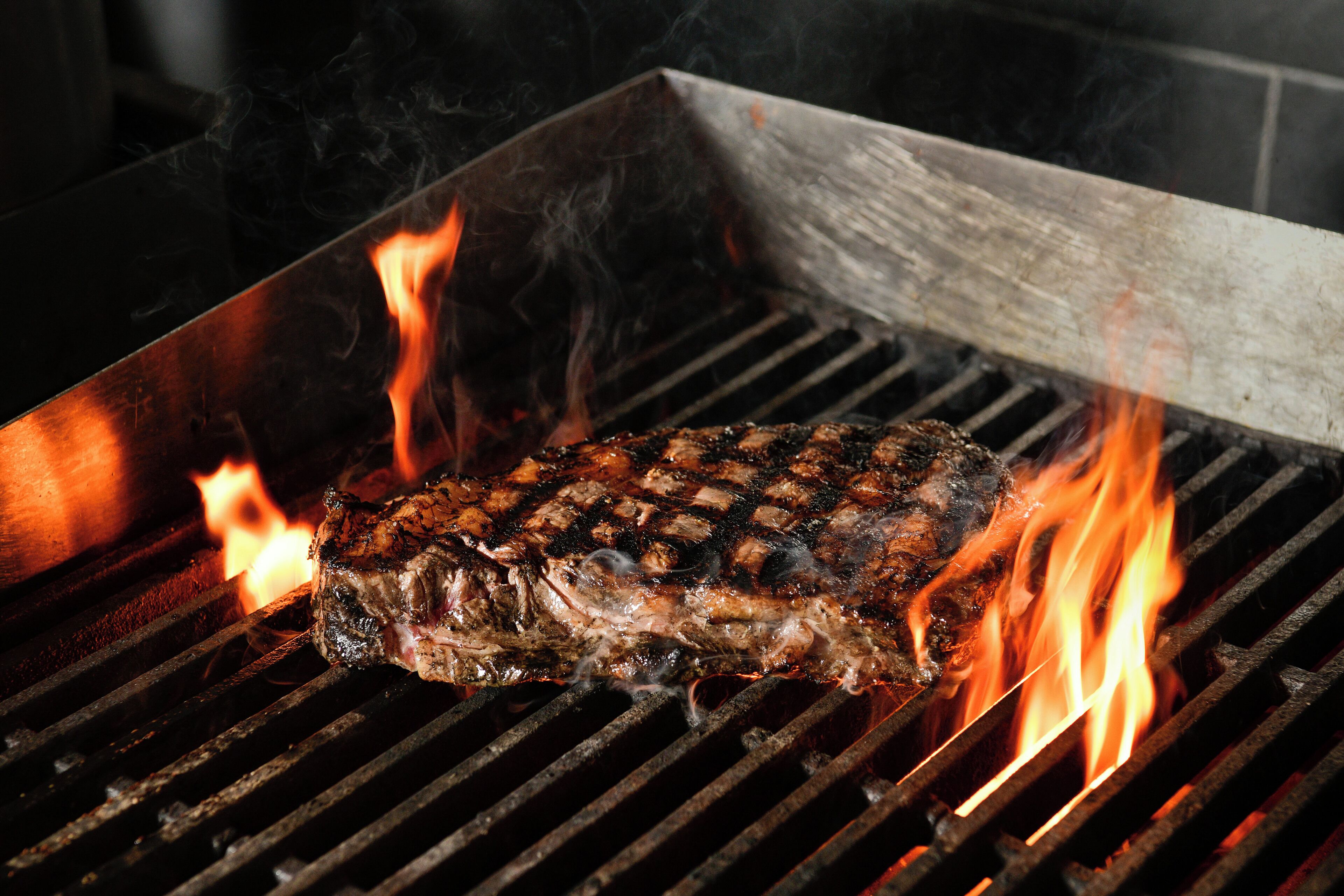 Un steak grillé sur un barbecue, avec des flammes apparentes.