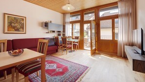 Una sala de estar acogedora con techo de madera, un sofá rojo, una mesa de comedor con sillas, un televisor y un amplio ventanal con cortinas.