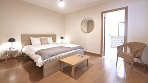 A bedroom with a bed, bedside tables, a wooden bench, a wicker chair, and a round mirror on the wall. - Idyllic Lisbon Apartments With Amazing Courtyard (Lisboa)