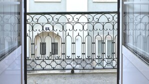 A view from a balcony with a metal railing, a building with two windows, and a door leading to a wooden floor. - Idyllic Lisbon Apartments With Amazing Courtyard (Lisboa)