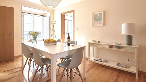 A dining area with a white table, four chairs, a vase with flowers, and a hanging light fixture. - Idyllic Lisbon Apartments With Amazing Courtyard (Lisboa)