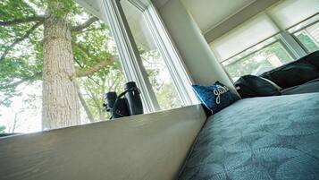 A room with a large window, a view of a tree, and a bed with patterned bedding.