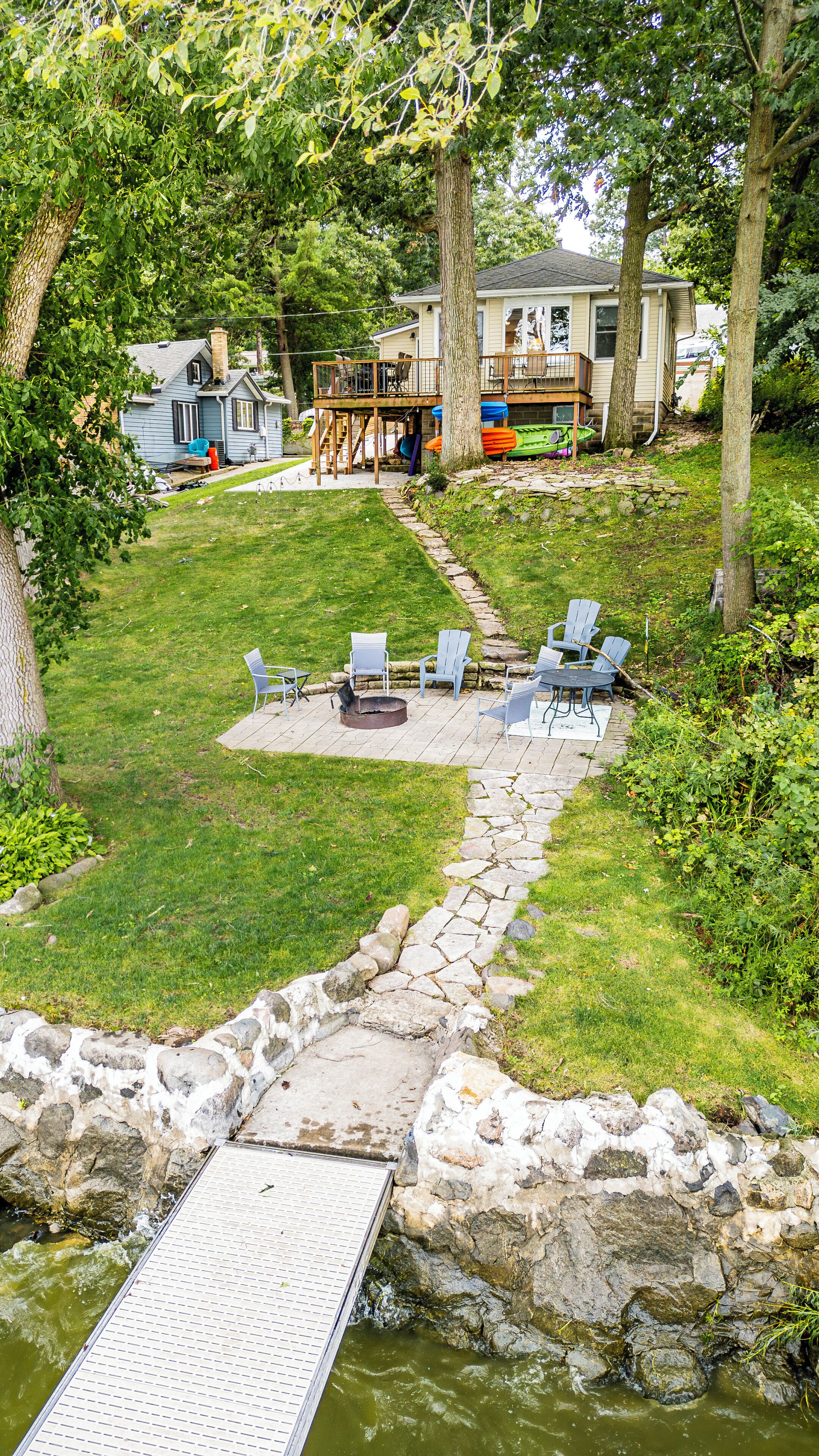 A backyard with a stone fire pit, outdoor seating, and kayaks stored under a deck.