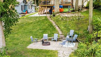 A backyard with a stone fire pit, outdoor seating, and kayaks stored under a deck.