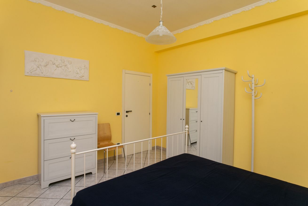 A bedroom with a bed, a dresser, a chair, a wardrobe, and a coat rack.