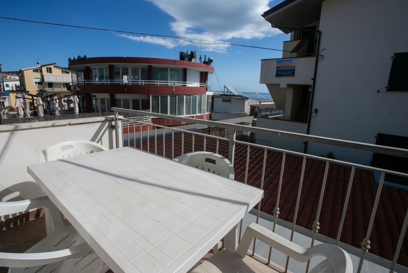 A balcony with a white table and chairs, a red building in the background, and a clear sky.