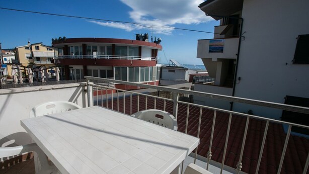 A balcony with a white table and chairs, a red building in the background, and a clear sky. - M116 - Marcelli, two-room apartment in the center and facing the sea (Marcelli)