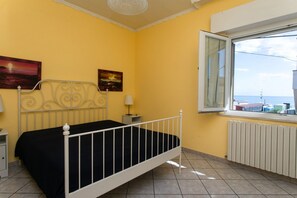 A room with a bed, two bedside tables, a window with a view, and two wall-mounted paintings. - M116 - Marcelli, two-room apartment in the center and facing the sea (Marcelli)
