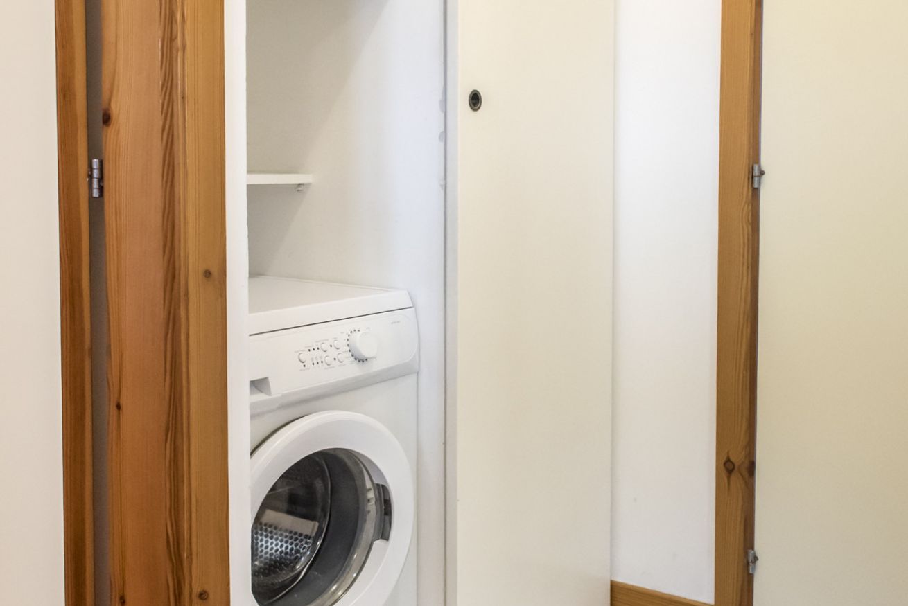 A small laundry area with a white washing machine, a wooden door frame, and a white wall.