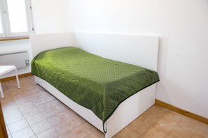 Een eenpersoonsbed met een groene sprei in een kamer met witte muren en een raam.